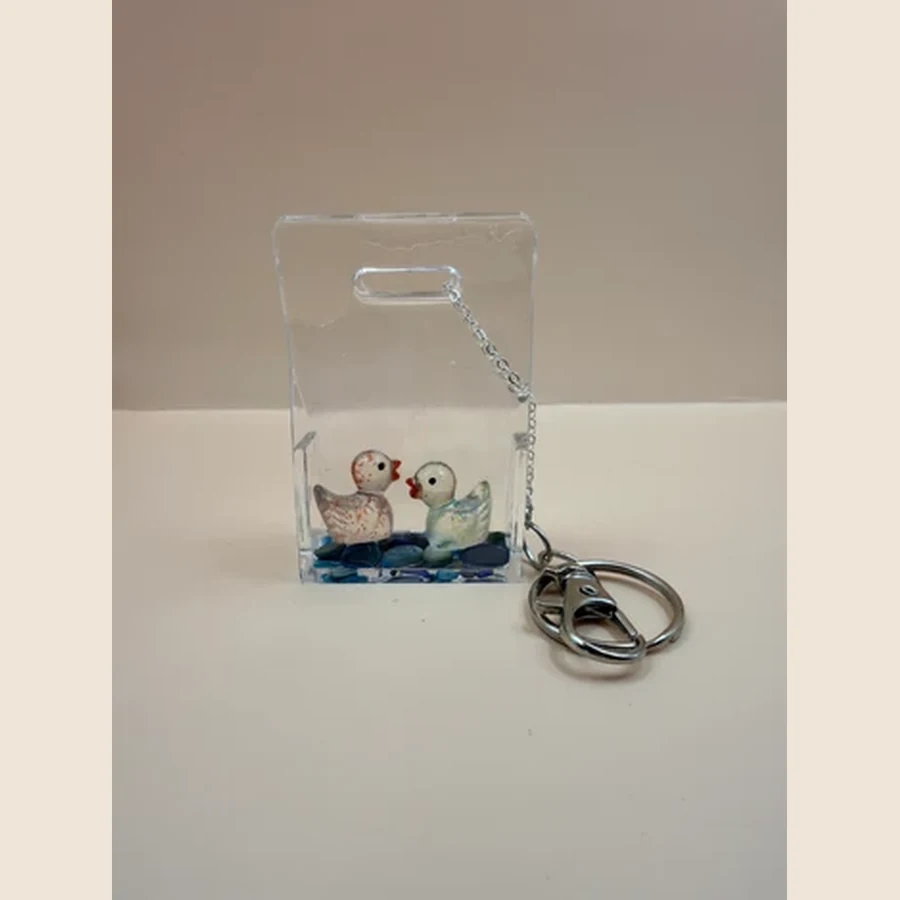Deze handgemaakte transparante sleutelhanger is een vrolijk en uniek item met twee schattige eendjes en kleine decoratieve steentjes aan de onderkant. Door de heldere uitstraling lijkt het net alsof de eendjes samen in een klein waterwereldje staan. Leuk voor aan je sleutelbos, tas, rugzak of als klein cadeautje voor iemand die dol is op vrolijke, handgemaakte accessoires.